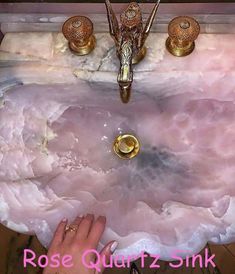 a woman's hand is touching the edge of a pink sink with gold faucets