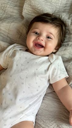 a smiling baby laying on top of a bed