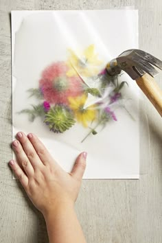 someone is painting flowers on a piece of paper with a paintbrush in their hand