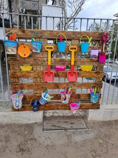 a wooden sign with buckets and shovels hanging on it's side next to a fence