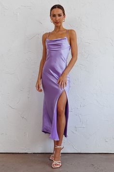 a woman standing in front of a white wall wearing a long purple dress with side slit