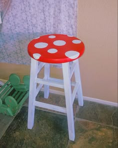 a red and white stool sitting in front of a window with polka dots on it