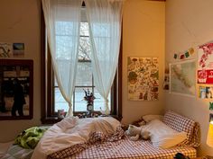 an unmade bed in front of a window with curtains on the windowsills