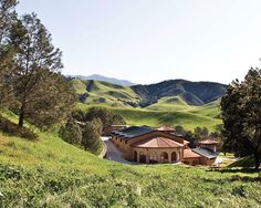 a large house sitting in the middle of a lush green field with mountains behind it