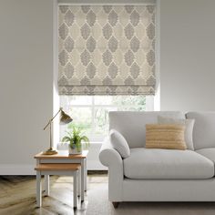 a white couch sitting under a window next to a table with a lamp on it