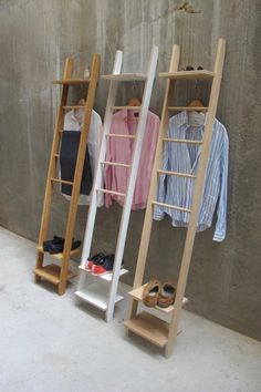 three wooden clothes racks with shoes and shirts hanging on them, in front of a concrete wall