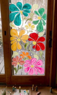 a window decorated with paper flowers and paint on the outside glass, next to some other crafting supplies