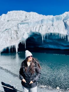 a woman standing in front of an ice - covered mountain with water and snow on the ground