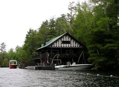 two boats are parked in front of a house on the water with trees around it