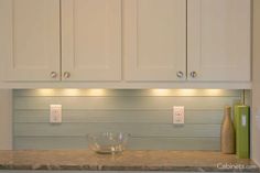 a kitchen with white cabinets and marble counter tops is lit by recessed lights above the sink