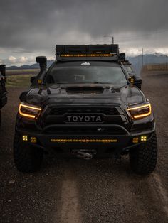 the front end of a black truck parked on a dirt road under a cloudy sky