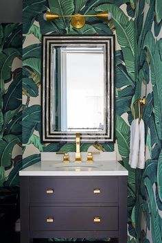 a bathroom vanity with a mirror and gold faucet in front of a palm leaf wallpaper