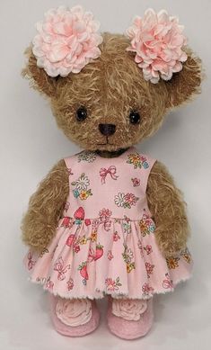 a brown teddy bear wearing a pink dress with flowers on it's head and shoes