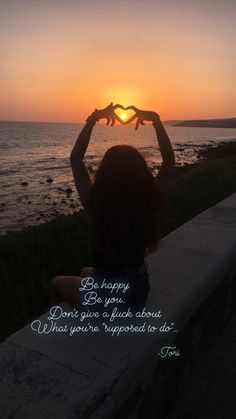 a person sitting on a ledge with their hands in the air and the sun setting behind them