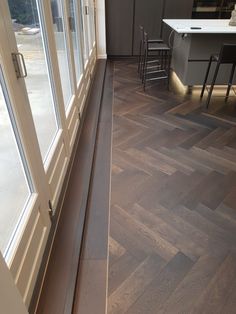 an empty room with wooden floors and glass doors on both sides, looking into the kitchen