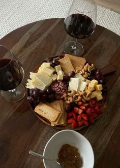 a wooden table topped with two wine glasses filled with red wine and assorted cheeses