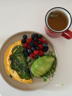 an omelet with spinach, berries and avocado on a plate next to a cup of coffee