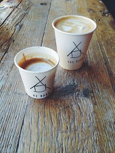 two cups of coffee sitting on top of a wooden table next to eachother