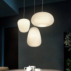 three lamps hanging from the ceiling above a table with two cups and saucers on it