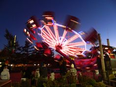 the ferris wheel is lit up at night with red and blue lights in the background