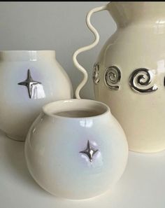 three white vases sitting on top of a table next to each other and one has a silver star in the middle