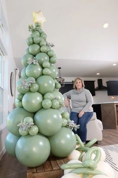 a woman sitting next to a christmas tree made out of balloons