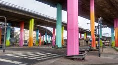 an empty bench in the middle of a street with colorful columns on either side of it