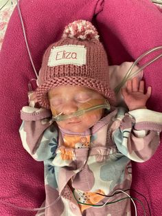 a baby with goggles and a hat on laying in a pink blanket wearing an oxygen tube