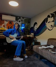 a man sitting on a couch playing a guitar in front of a wall with elvis presley pictures