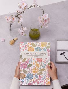 a person holding a book on top of a table next to a vase with flowers