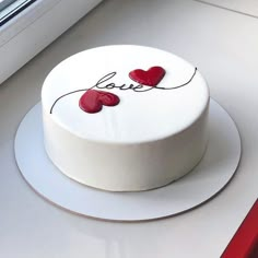 a white cake with two red hearts on it sitting next to a window sill