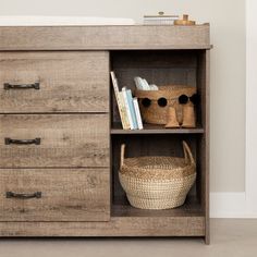 a wooden dresser with baskets and books on the bottom shelf, next to a crib