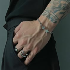 a man with tattoos on his arm wearing a black shirt and silver ring bracelets