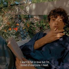 a man laying on top of a bed next to a plant and reading a book