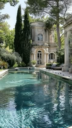 an outdoor swimming pool in front of a large house with trees and bushes around it