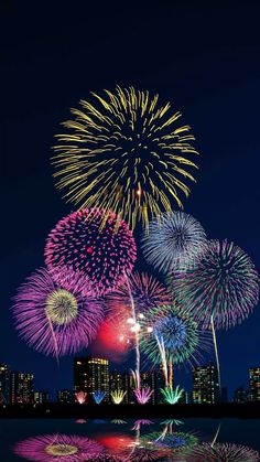 fireworks are lit up in the night sky with buildings and water reflecting on the surface