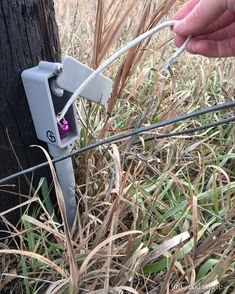 a hand is holding a wire and plugged into a telephone pole in the grass