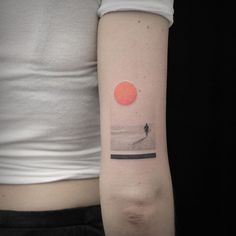 a woman with a small tattoo on her arm that has an image of a person walking in the water at sunset