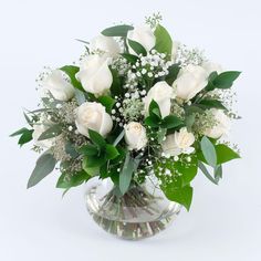 a vase filled with white roses and greenery