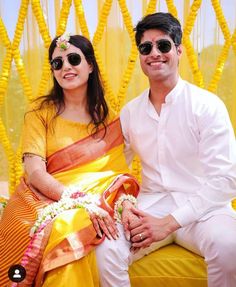 a man and woman sitting next to each other on a yellow chair with flowers in their hair