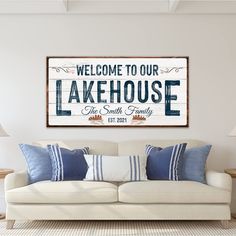 a living room with a white couch and wooden sign on the wall that says welcome to our lakehouse