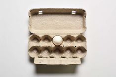 an egg in a carton on a white surface with the lid open and six eggs inside