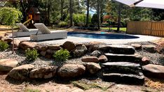 a backyard with a pool, rocks and an umbrella