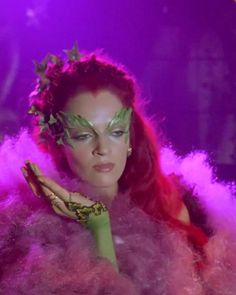 a woman with red hair and green makeup is dressed in purple feathers, holding a banana