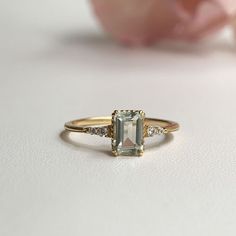 an engagement ring with a green emerald surrounded by three white diamonds on a table next to a pink rose