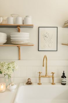 a white kitchen sink with gold faucet and open shelving on the wall