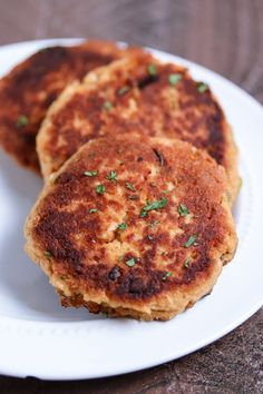 three crab cakes on a white plate with parsley sprinkled on top, ready to be eaten