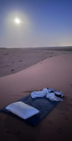 an empty sleeping bag on the beach at night with the moon in the sky above it