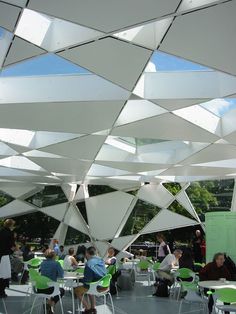 a group of people sitting at tables under a large white structure with mirrors hanging from it's ceiling