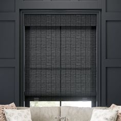 a living room with a couch and window covered in black roman blind shades on the windowsill